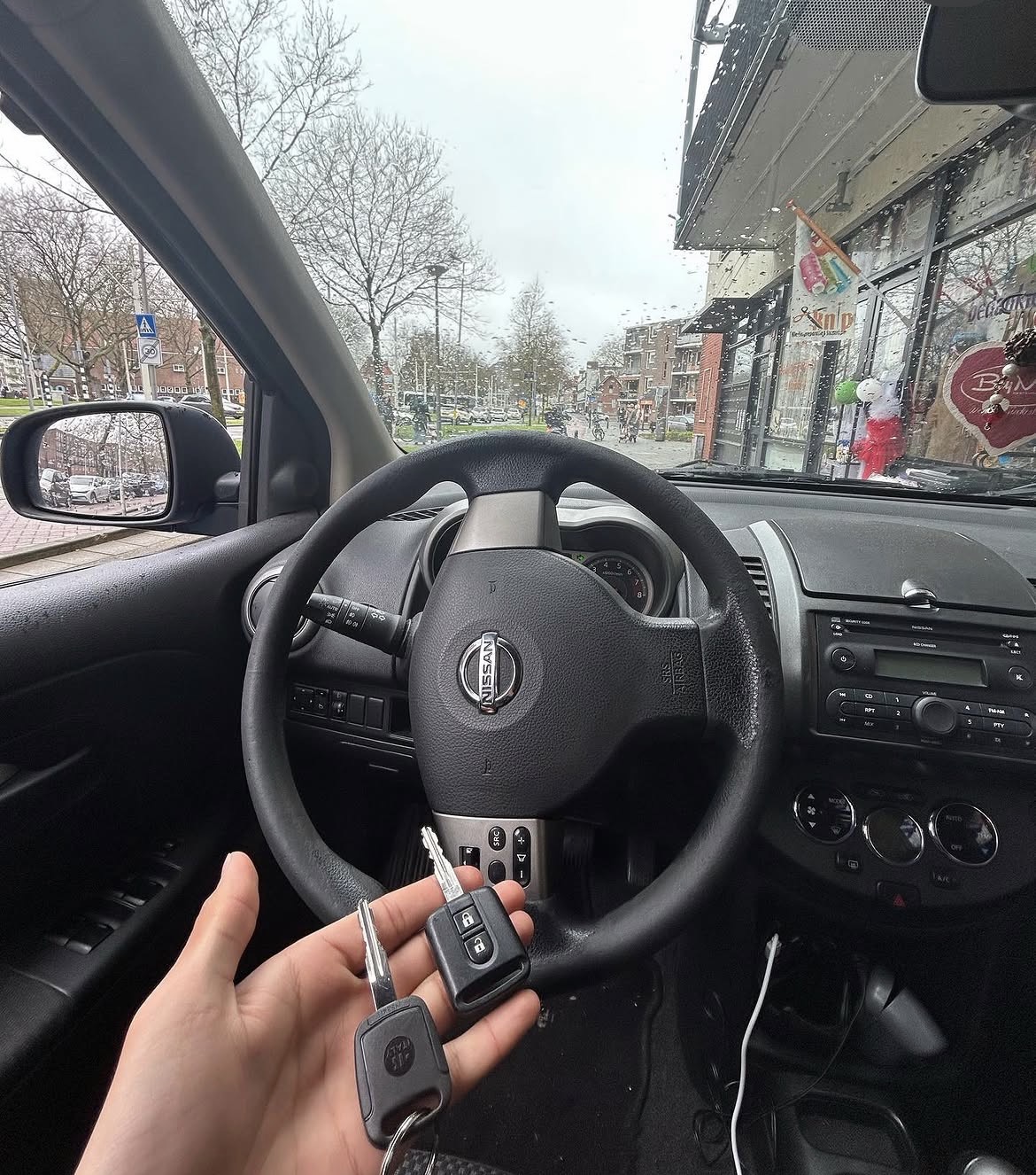 Twee autosleutels in een hand in een Nissan, gezien vanuit de bestuurdersstoel