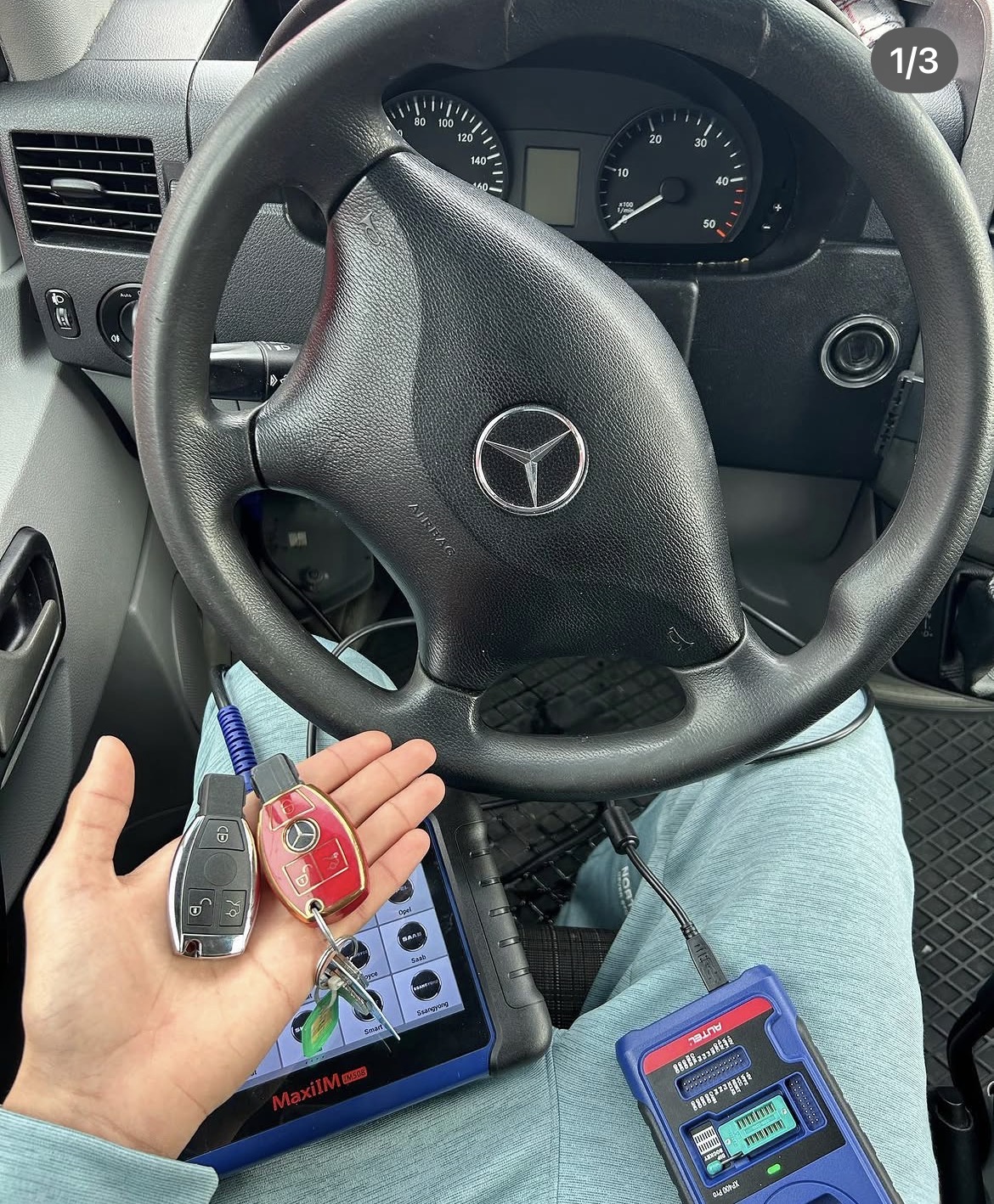 Twee autosleutels in een hand bij een Mercedes-bestelwagen met programmeertablet op schoot